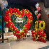 Heart shape anniversary balloon decoration with red and gold balloons and number setup in Bhopal